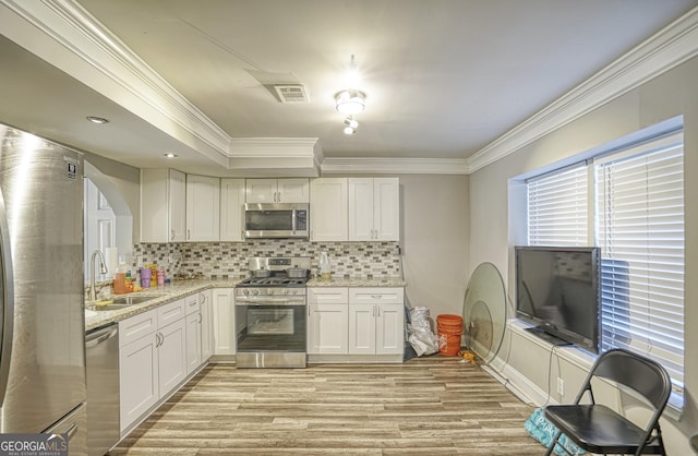 kitchen with sink, stainless steel appliances, light stone counters, decorative backsplash, and white cabinets