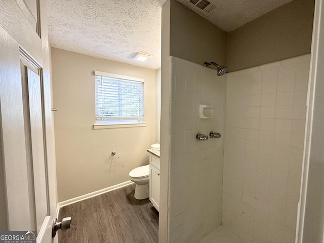 bathroom with hardwood / wood-style floors, vanity, toilet, a textured ceiling, and a tile shower