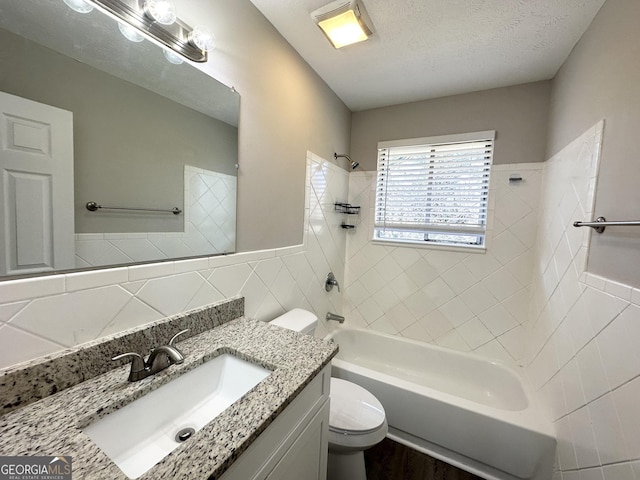 full bathroom featuring vanity, tiled shower / bath combo, toilet, a textured ceiling, and tile walls