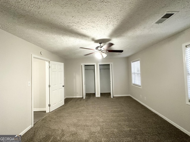 unfurnished bedroom featuring ceiling fan, dark carpet, a textured ceiling, and multiple closets