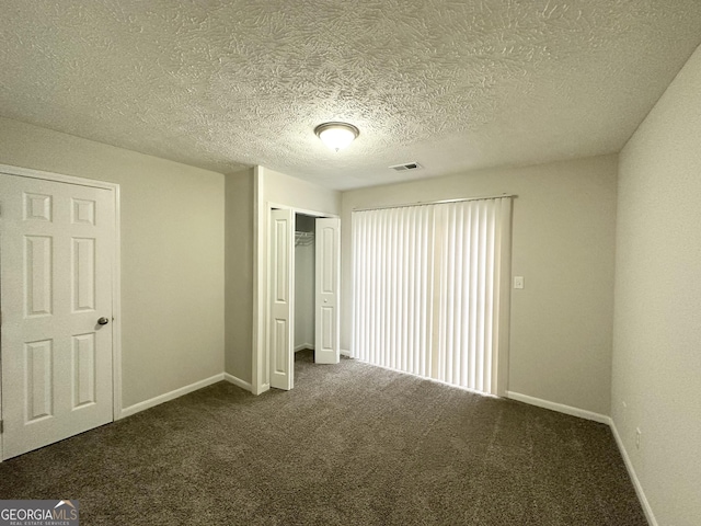 unfurnished bedroom with a closet, dark carpet, and a textured ceiling