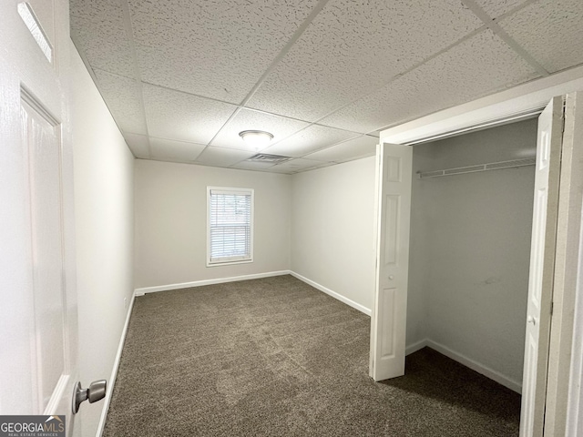 unfurnished bedroom featuring dark colored carpet, a paneled ceiling, and a closet