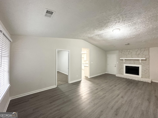 unfurnished living room with a textured ceiling, dark wood-type flooring, a stone fireplace, and lofted ceiling