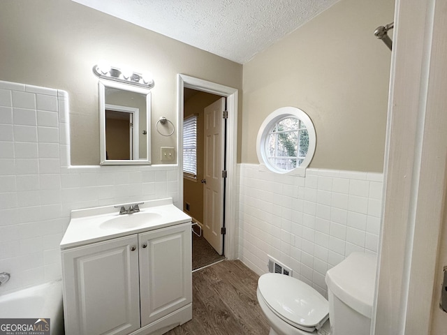 bathroom featuring vanity, hardwood / wood-style flooring, toilet, tile walls, and a textured ceiling