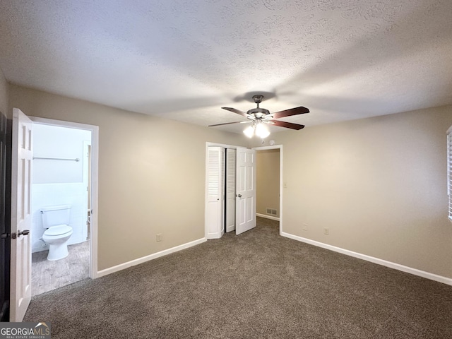 unfurnished bedroom featuring connected bathroom, ceiling fan, a textured ceiling, and dark colored carpet