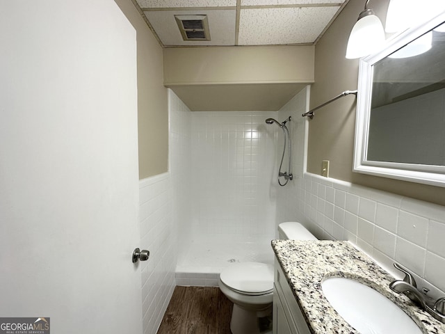 bathroom with vanity, tiled shower, hardwood / wood-style flooring, tile walls, and toilet