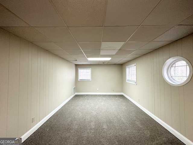 basement with carpet, a paneled ceiling, and wooden walls