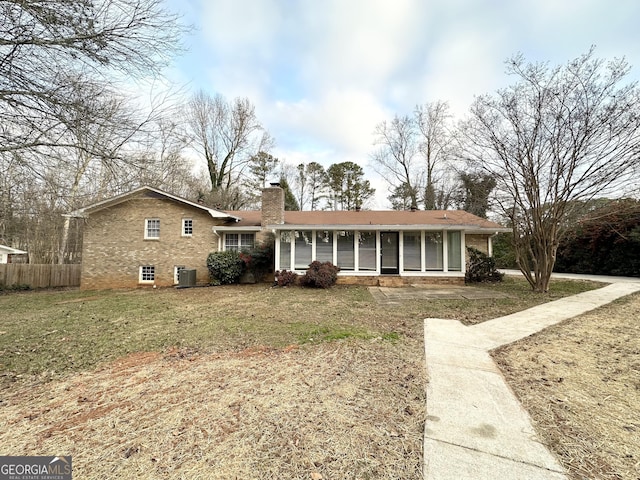 ranch-style home with a front yard, central air condition unit, and a sunroom