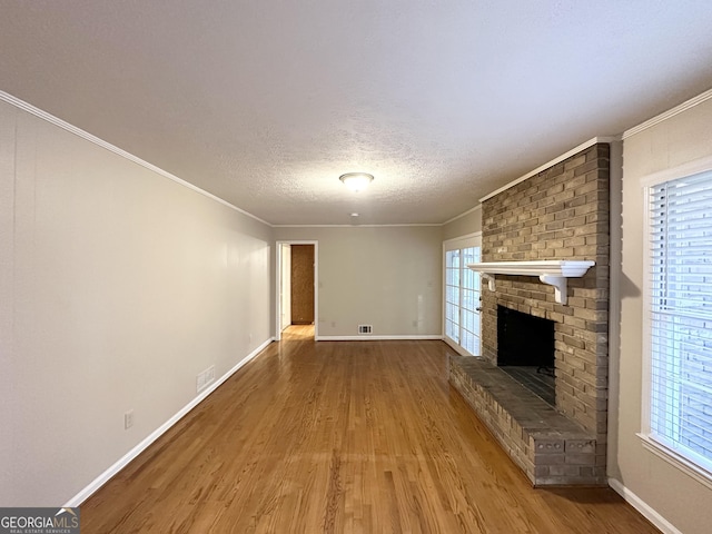 unfurnished living room featuring hardwood / wood-style flooring, a healthy amount of sunlight, a textured ceiling, and a brick fireplace