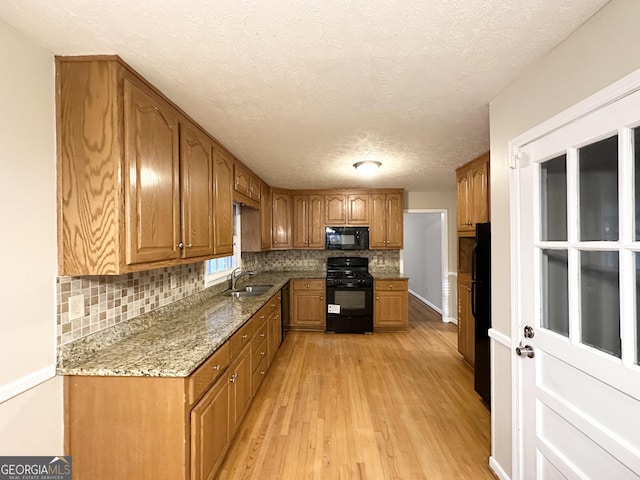 kitchen featuring a textured ceiling, sink, black appliances, light hardwood / wood-style flooring, and stone counters