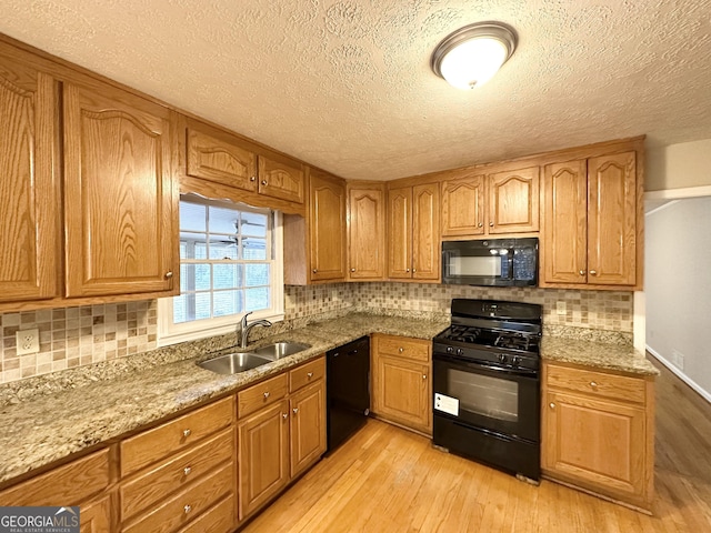 kitchen with light stone countertops, sink, black appliances, and light hardwood / wood-style flooring