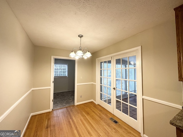 unfurnished dining area featuring light wood-type flooring, a textured ceiling, a wealth of natural light, and a chandelier