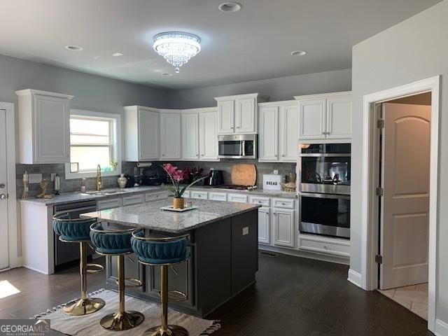 kitchen with a kitchen bar, sink, white cabinetry, a center island, and black appliances