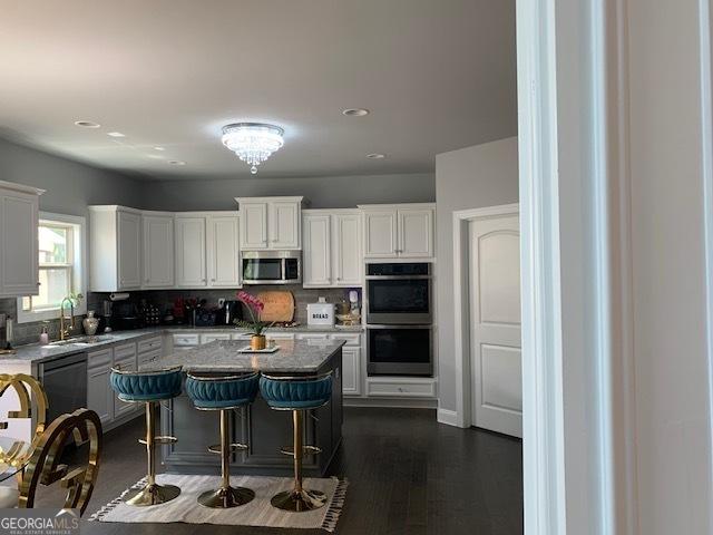 kitchen featuring a kitchen island, double oven, white cabinetry, sink, and a breakfast bar area