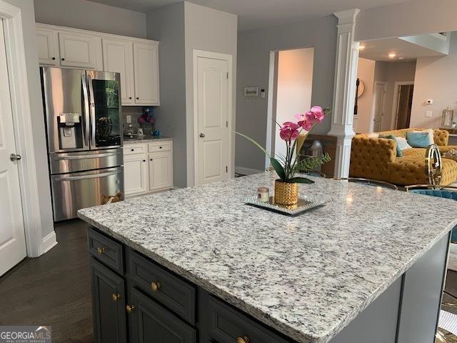 kitchen featuring decorative columns, white cabinetry, stainless steel fridge, dark hardwood / wood-style flooring, and light stone countertops