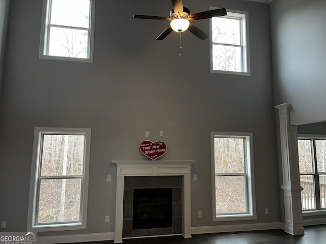 unfurnished living room with a high ceiling, a tiled fireplace, wood-type flooring, and ceiling fan