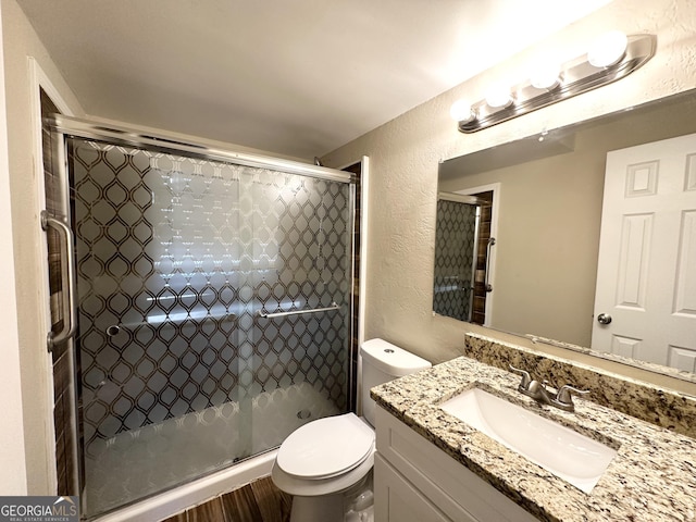 bathroom with wood-type flooring, vanity, toilet, and a shower with door