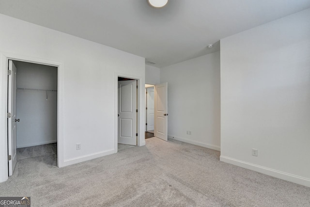 unfurnished bedroom with a walk in closet, light colored carpet, and a closet