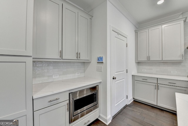 kitchen with hardwood / wood-style flooring, stainless steel microwave, ornamental molding, and tasteful backsplash