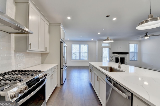 kitchen with light stone countertops, appliances with stainless steel finishes, wall chimney exhaust hood, sink, and pendant lighting