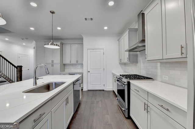 kitchen with sink, hanging light fixtures, stainless steel appliances, wall chimney range hood, and light stone counters