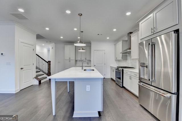 kitchen with wall chimney exhaust hood, stainless steel appliances, sink, pendant lighting, and an island with sink