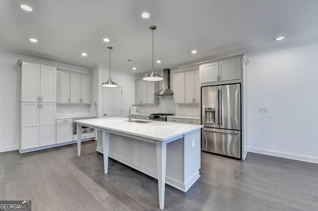 kitchen featuring a kitchen island with sink, sink, wall chimney exhaust hood, appliances with stainless steel finishes, and decorative light fixtures