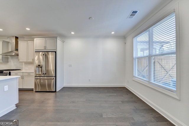 kitchen with stainless steel appliances, wall chimney range hood, dark hardwood / wood-style flooring, white cabinets, and ornamental molding