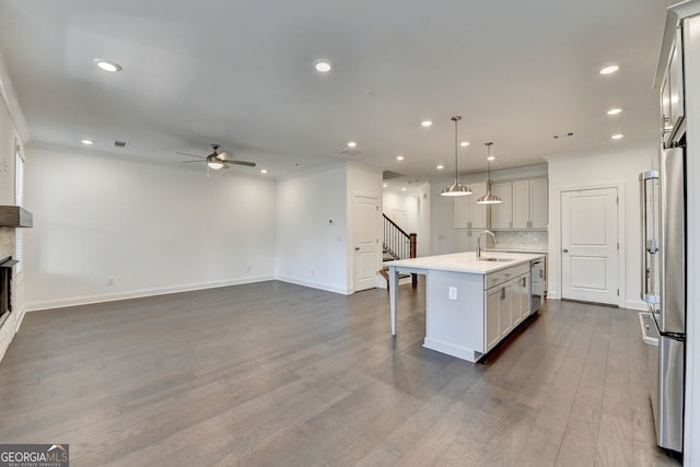 kitchen featuring decorative backsplash, a kitchen island with sink, ceiling fan, pendant lighting, and dark hardwood / wood-style floors