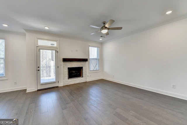 unfurnished living room with a stone fireplace, ceiling fan, dark wood-type flooring, and crown molding