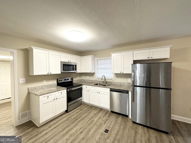 kitchen with sink, light stone counters, appliances with stainless steel finishes, white cabinets, and light wood-type flooring