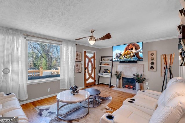 living room featuring a tile fireplace, ceiling fan, crown molding, a textured ceiling, and light hardwood / wood-style flooring