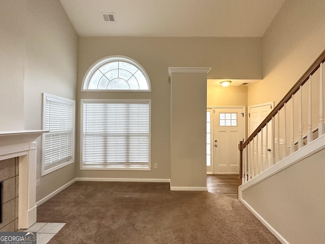 foyer entrance with a tile fireplace, a towering ceiling, dark colored carpet, and a wealth of natural light