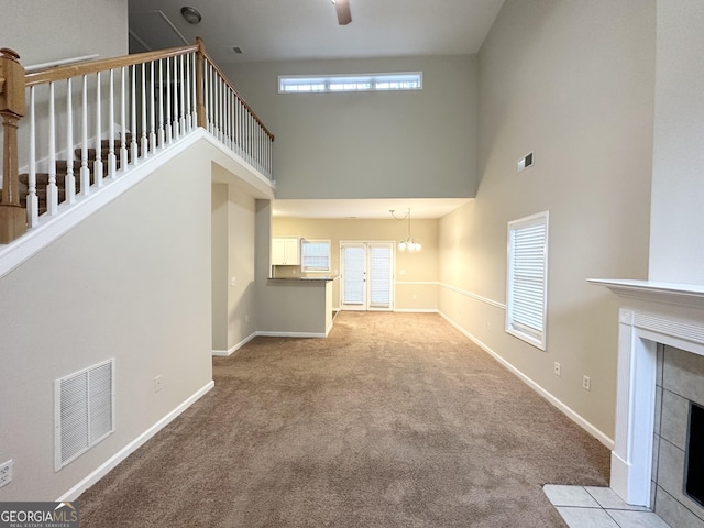 unfurnished living room featuring a fireplace, a high ceiling, ceiling fan with notable chandelier, and light carpet