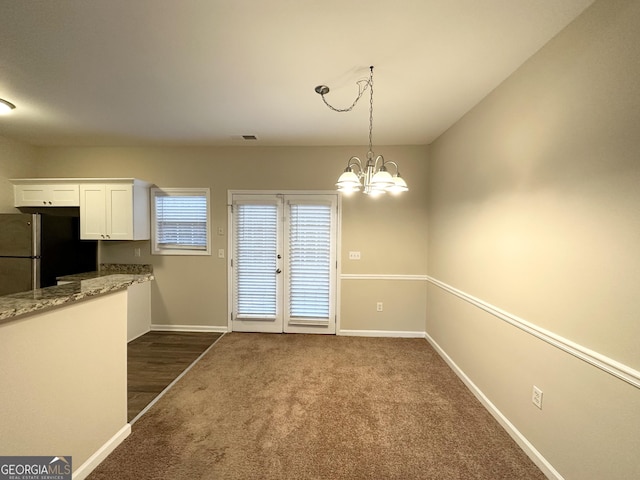 unfurnished dining area featuring a chandelier and dark carpet