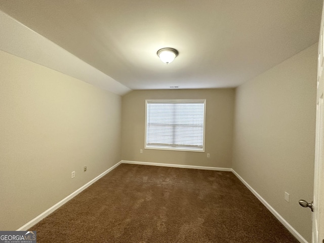 empty room featuring vaulted ceiling and dark colored carpet