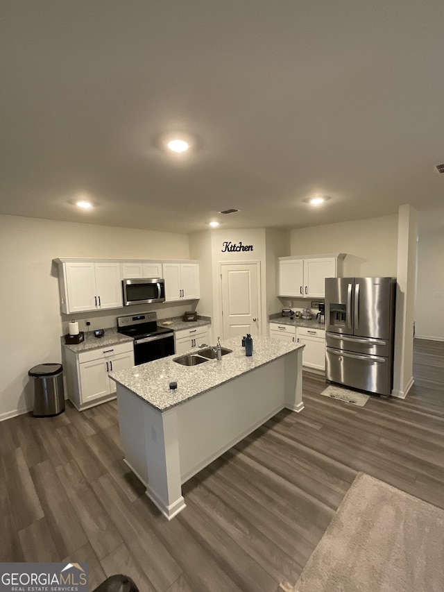 kitchen featuring a center island with sink, sink, appliances with stainless steel finishes, light stone counters, and white cabinetry