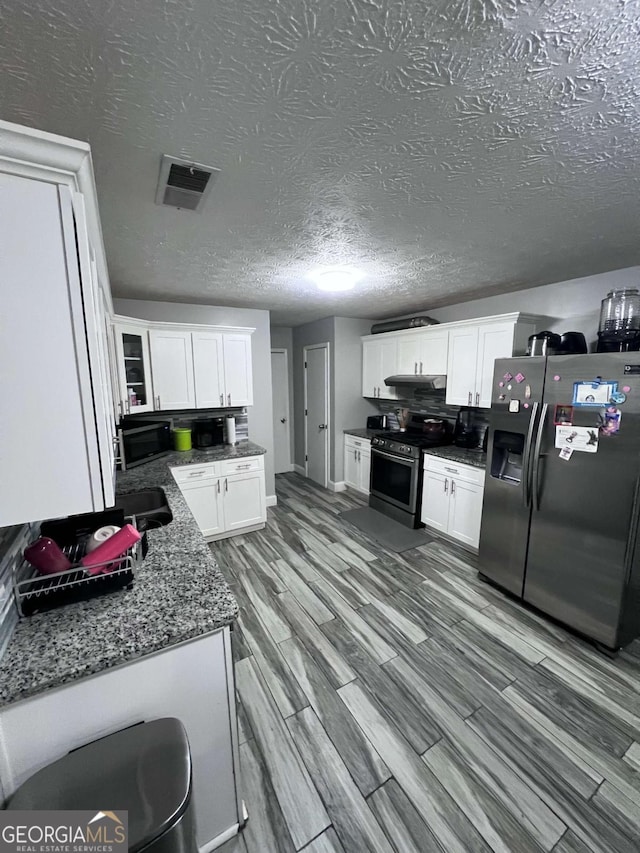 kitchen featuring backsplash, dark stone counters, white cabinets, light hardwood / wood-style floors, and stainless steel appliances