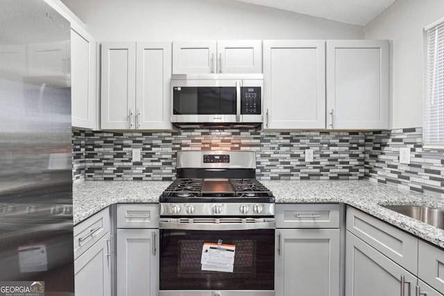 kitchen featuring light stone countertops, lofted ceiling, appliances with stainless steel finishes, and tasteful backsplash