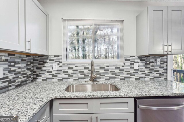 kitchen with decorative backsplash, dishwasher, light stone counters, and sink