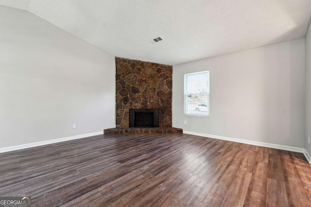 unfurnished living room with a fireplace, a textured ceiling, vaulted ceiling, and dark wood-type flooring