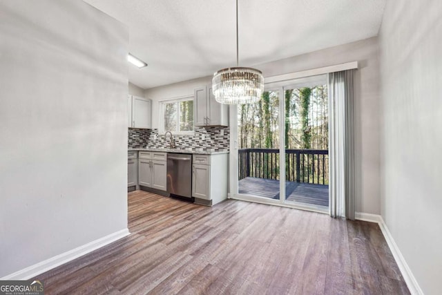 kitchen featuring pendant lighting, a healthy amount of sunlight, stainless steel dishwasher, tasteful backsplash, and light hardwood / wood-style floors