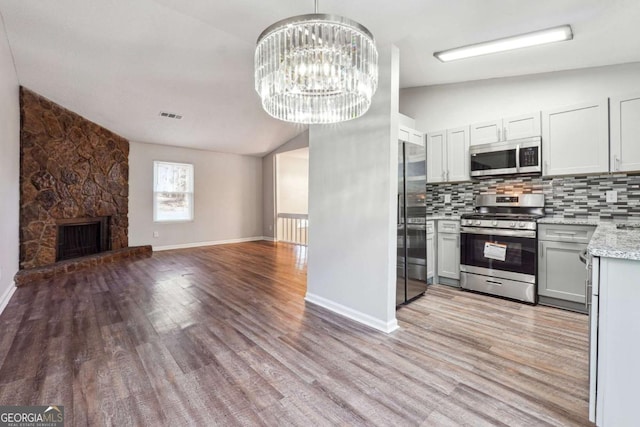 kitchen featuring stainless steel appliances, an inviting chandelier, lofted ceiling, decorative backsplash, and light wood-type flooring