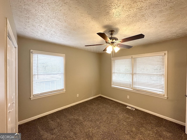 empty room with ceiling fan, dark carpet, and a textured ceiling