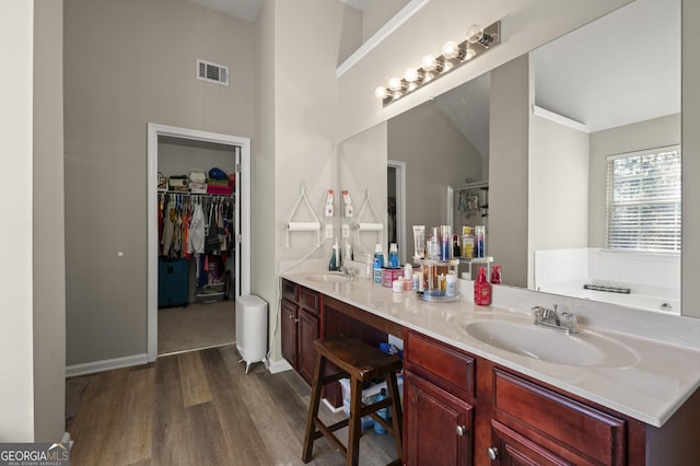 bathroom featuring vanity, wood-type flooring, a tub to relax in, and lofted ceiling