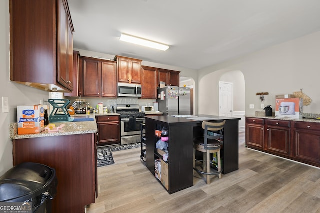 kitchen with light stone countertops, a center island, a kitchen bar, stainless steel appliances, and light hardwood / wood-style floors