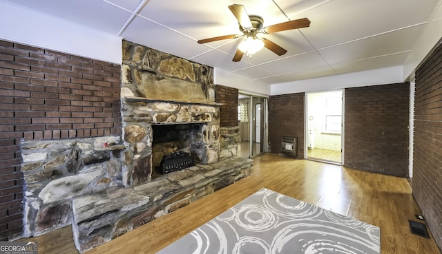 living room with hardwood / wood-style floors, ceiling fan, a stone fireplace, and brick wall