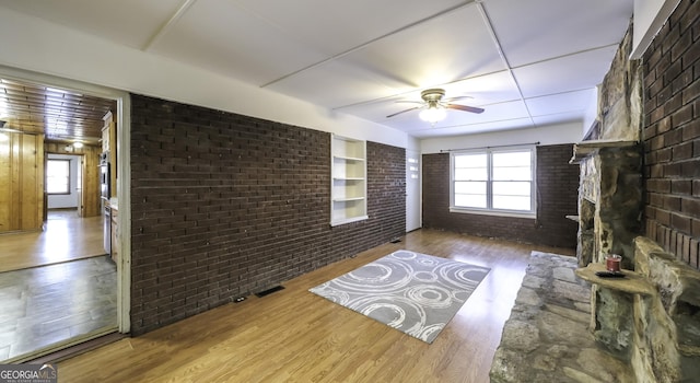 unfurnished living room featuring ceiling fan, brick wall, and light hardwood / wood-style flooring