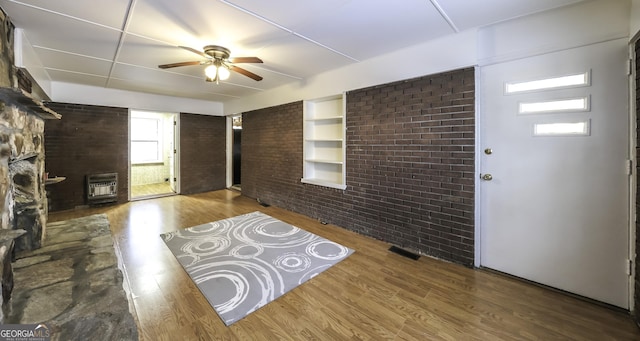 entrance foyer featuring brick wall, heating unit, ceiling fan, hardwood / wood-style flooring, and a fireplace