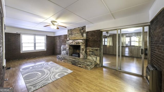 living room featuring brick wall, heating unit, ceiling fan, hardwood / wood-style flooring, and a stone fireplace